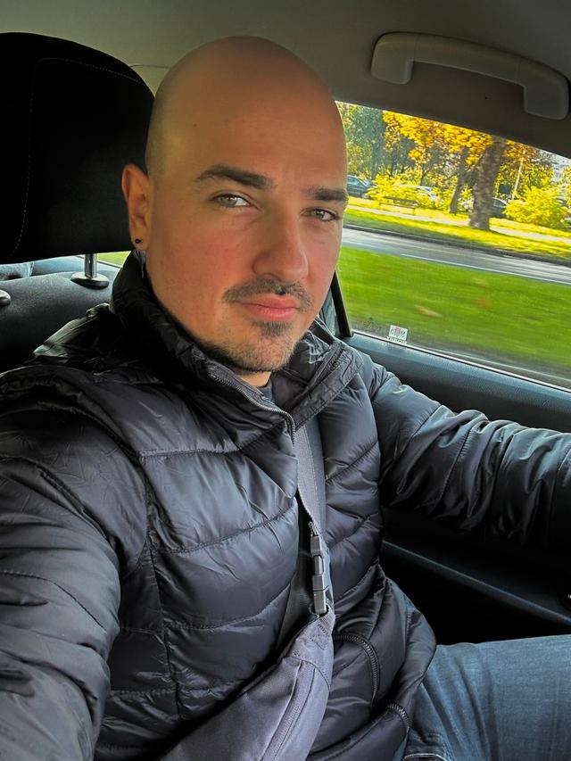 Dušan driving a car, wearing a black jacket.